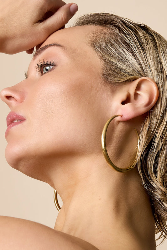 Close-up profile of woman wearing sculpted gold hoop earring showcasing youthful minimalist style