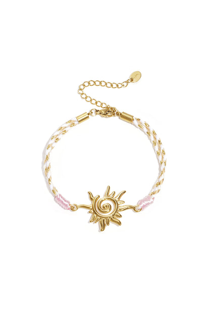 Close-up of cream and gold braided rope bracelet with gold heart charm on white background