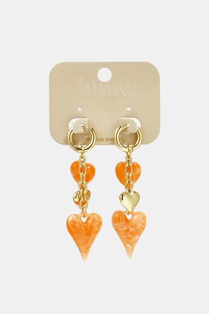 Gold dangle earrings featuring orange marbled heart charms and gold heart accents on a branded jewelry card.