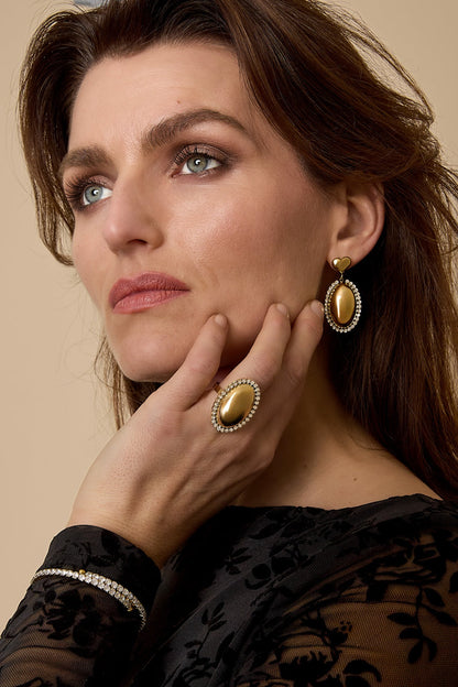 Woman wearing elegant gold drop earrings and matching ring with oval rhinestone design, dressed in a black floral sheer top