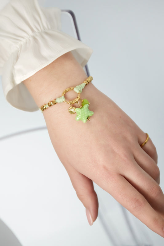 Close-up of bracelet worn on wrist showing green starfish charm and gold beads with white sleeve