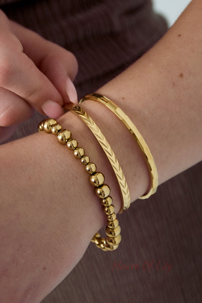 Close-up of woman's wrist wearing three gold-tone bracelets including an embossed bangle bracelet against brown top
