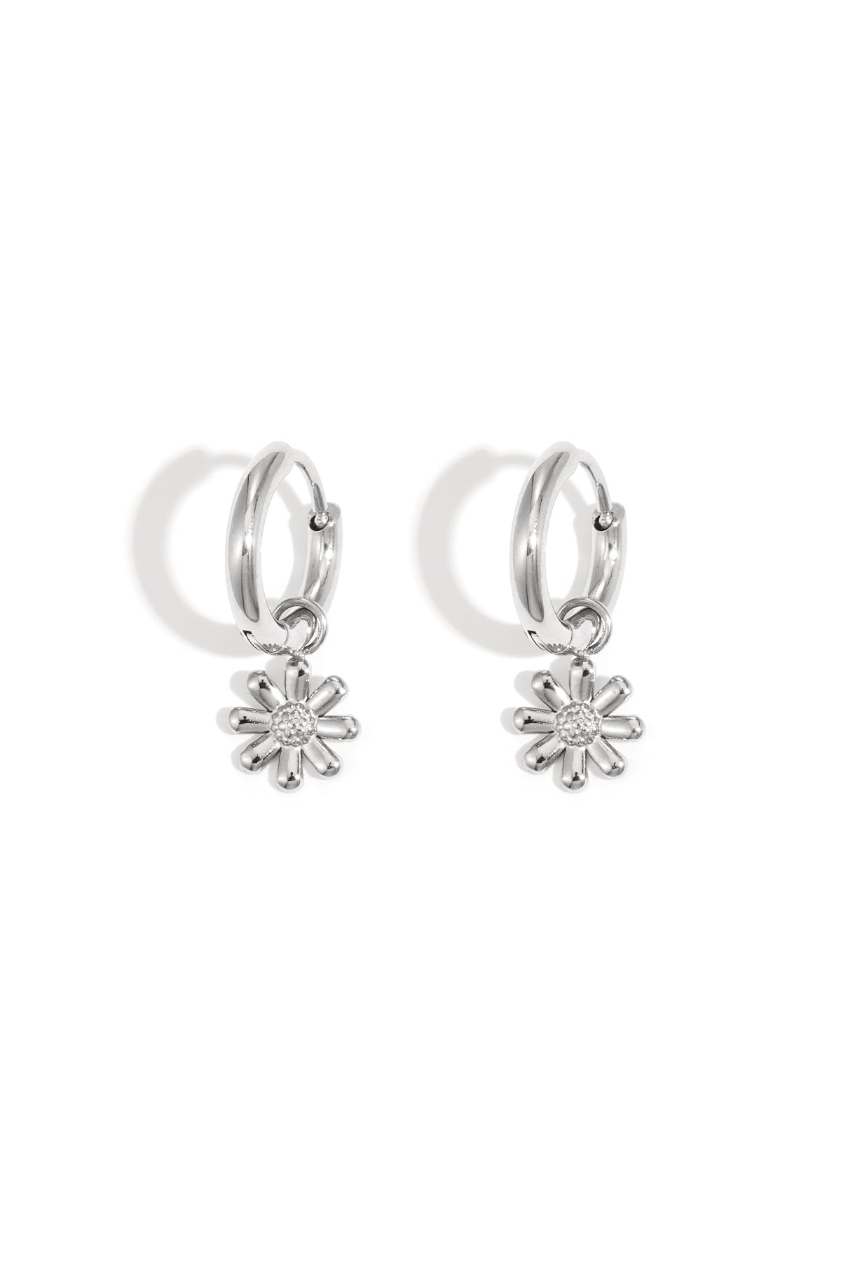 Pair of silver hoop earrings featuring dangling daisy flower charms, placed on white background