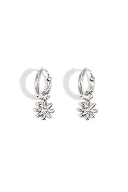 Pair of silver hoop earrings featuring dangling daisy flower charms, placed on white background