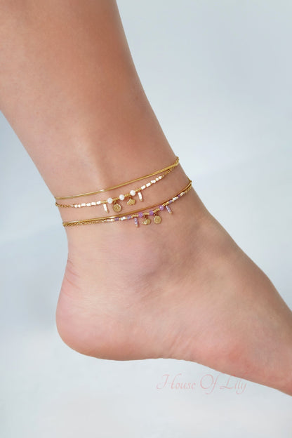Close-up view of anklets with gold chains, pastel beads, and charms worn on ankle against light background