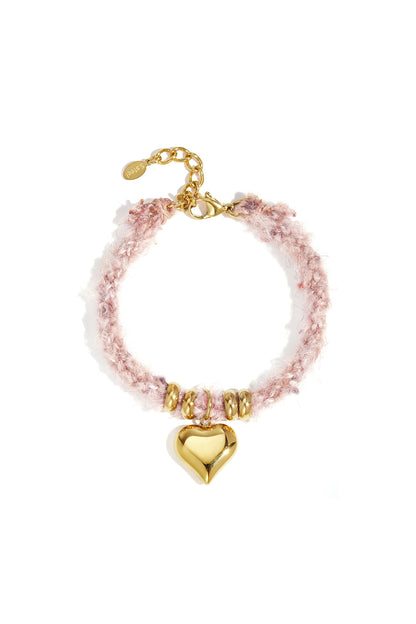 Close-up of a pink knitted bracelet with gold heart charm and gold bead accents on a white background