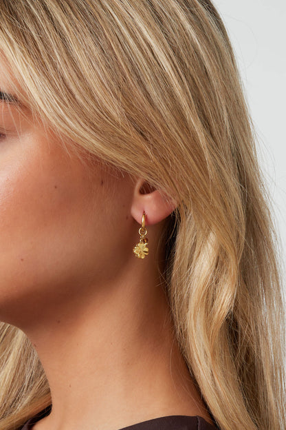 Model wearing gold hoop earrings featuring four-leaf clover charm and yellow bead