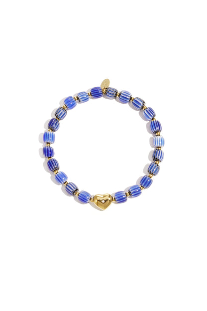 Blue and white striped beaded bracelet with gold heart charm laid flat on white background