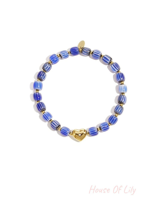 Blue and white striped beaded bracelet with gold heart charm laid flat on white background