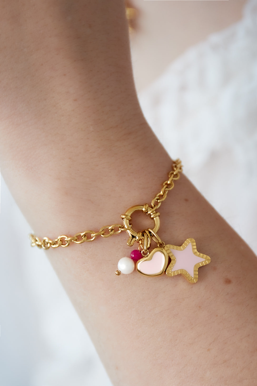 Close-up view of gold plated charm bracelet worn on wrist featuring star, heart, and bead charms