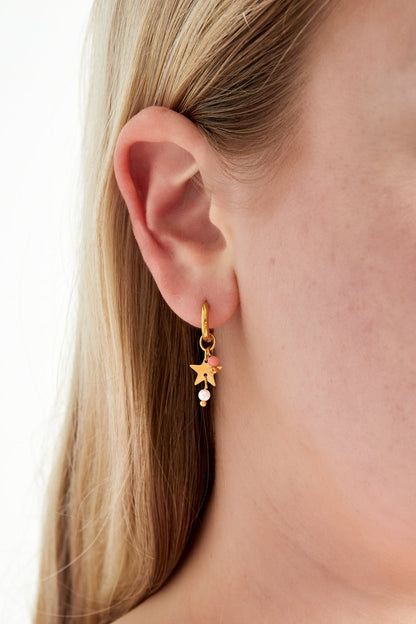 Close-up of model wearing one gold hoop earring featuring a star charm, pink bead, and pearl drop