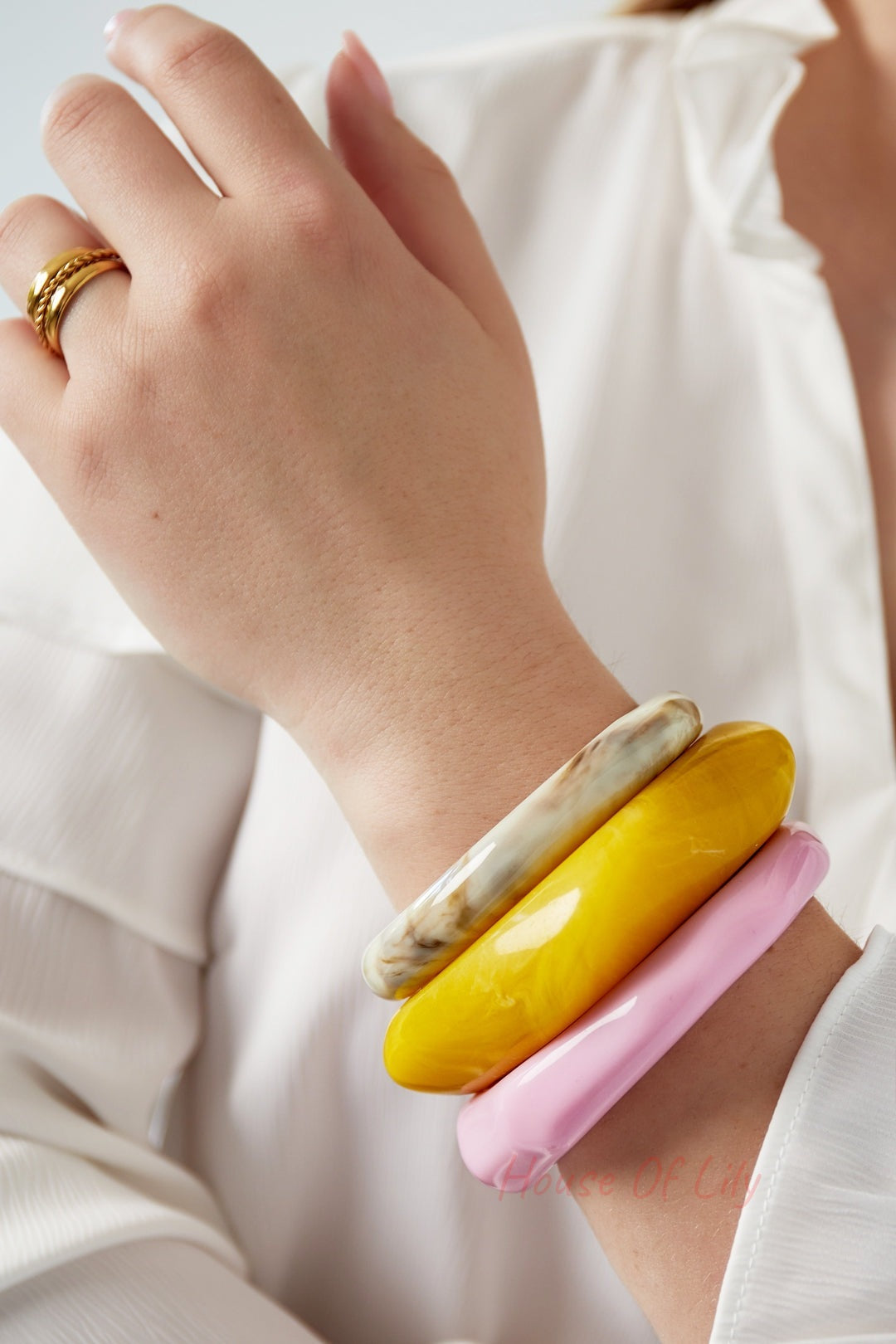 Close-up of a woman's wrist wearing three chunky resin bangles in beige, yellow, and pink, paired with a white blouse