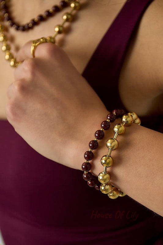 Close-up of model's wrist wearing burgundy and gold-tone double layered beaded bracelets with matching necklace and ring