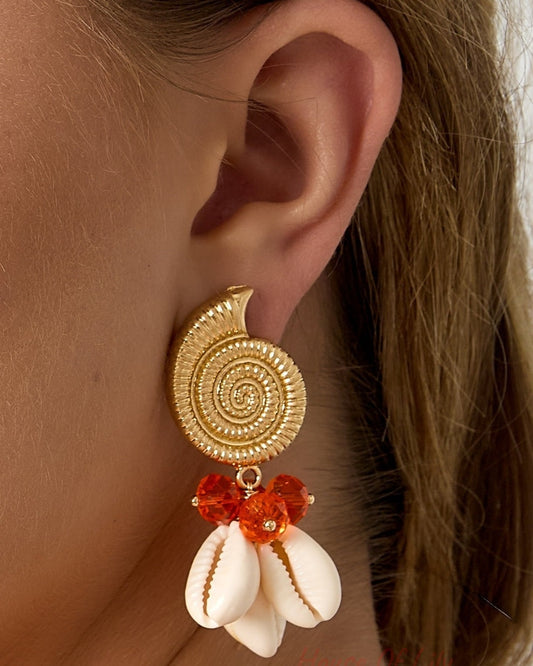 Close-up side view of woman wearing gold spiral shell earrings with orange glass beads and cowry shells