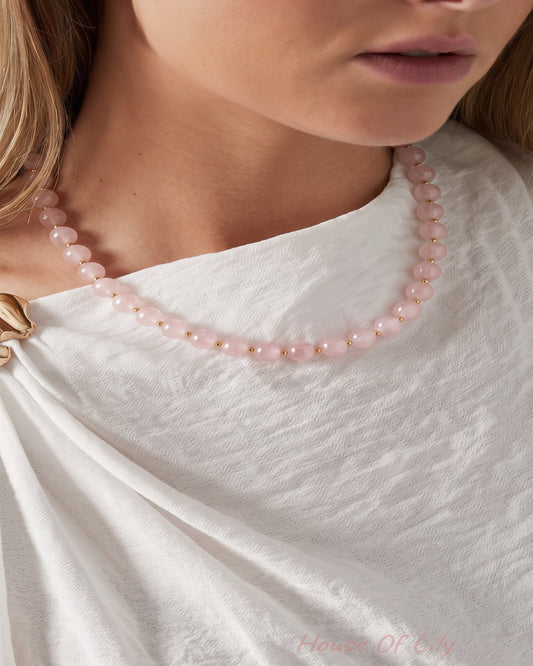 A close-up of a model wearing a delicate pink beaded necklace with small pearl-like accents, styled with a white draped top.