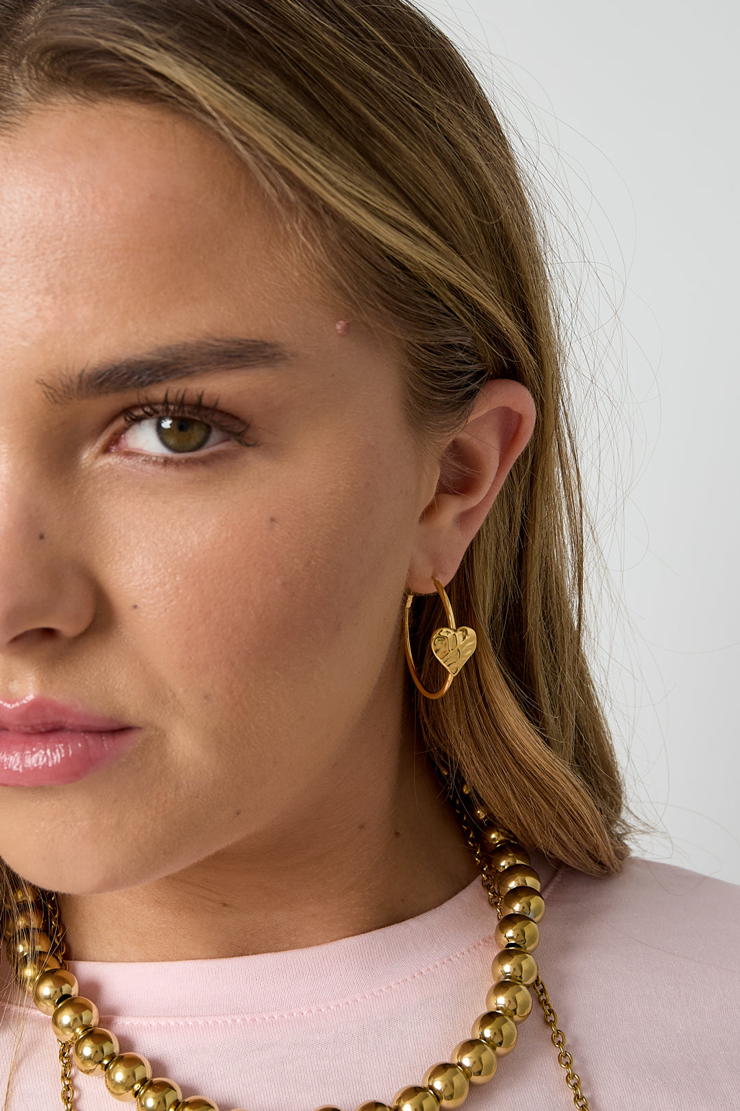 Close-up front view of woman wearing gold textured heart hoop earrings