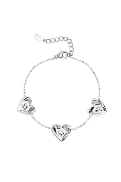 Silver tone charm bracelet with three sculpted heart-shaped charms linked by delicate chain on white background