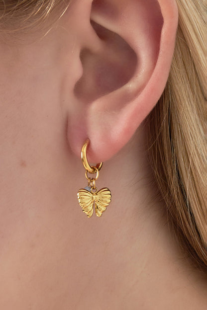 Close-up of butterfly charm gold hoop earring with a gray bead worn on an ear