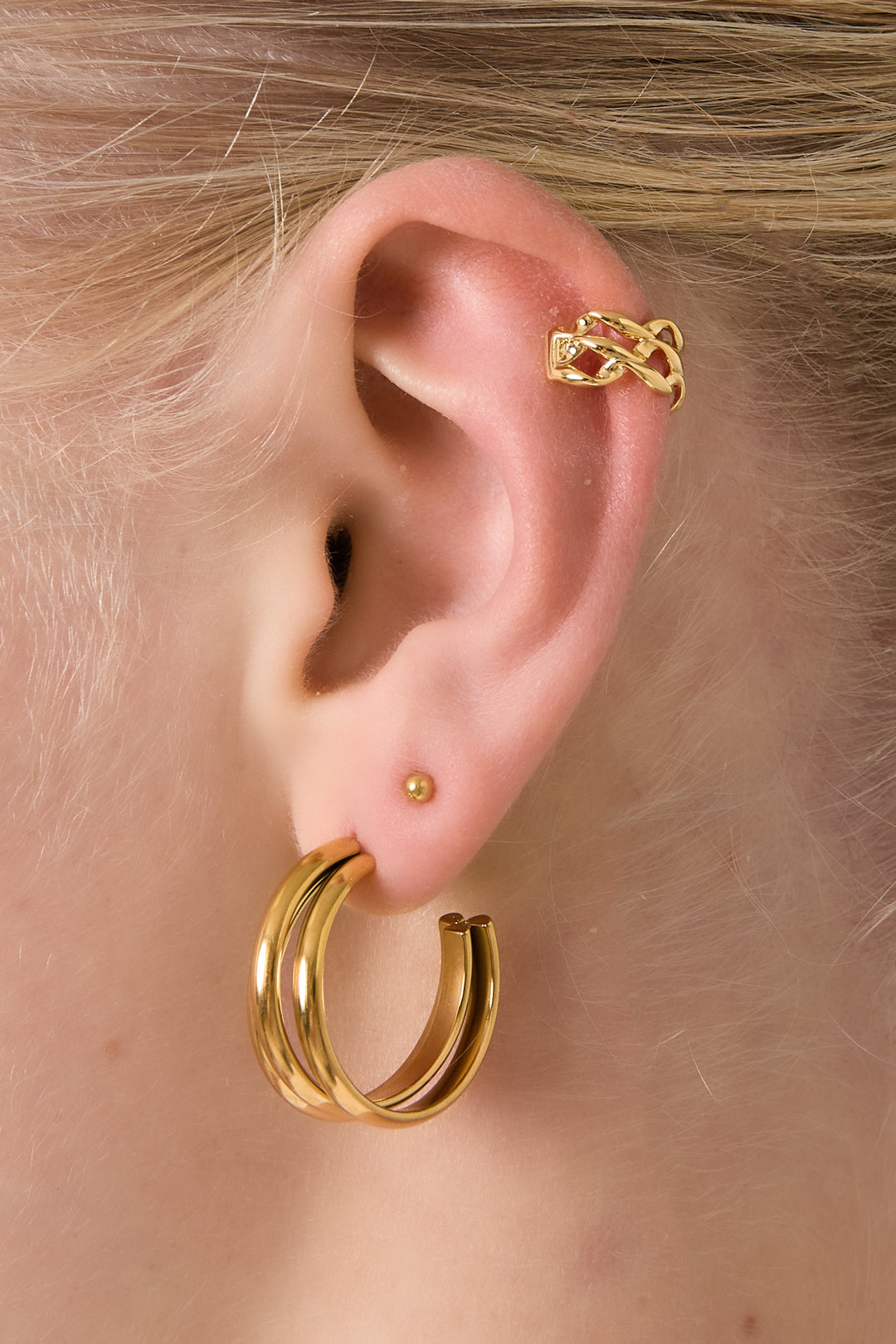 Model wearing a gold twisted chain ear cuff on upper ear and matching gold hoop earrings, showing soft youthful styling