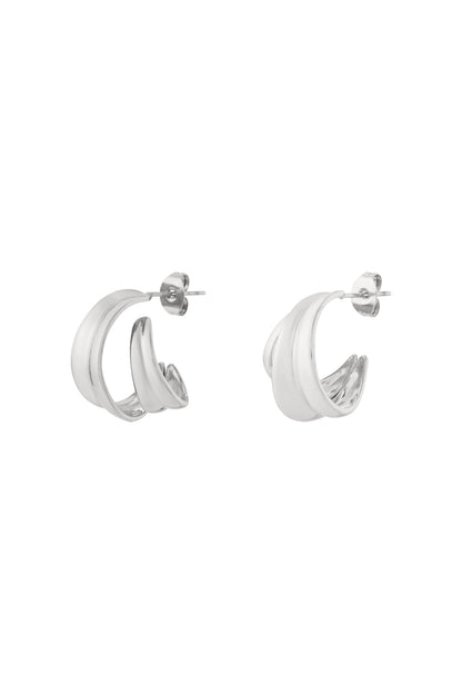 A pair of polished silver-tone curved sculptural hoop earrings with a smooth double-band design on a white background