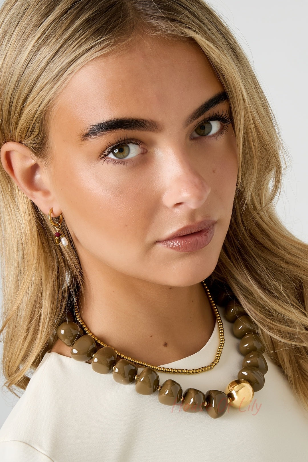Portrait of a blonde woman wearing a chunky brown beaded necklace and gold accent earrings