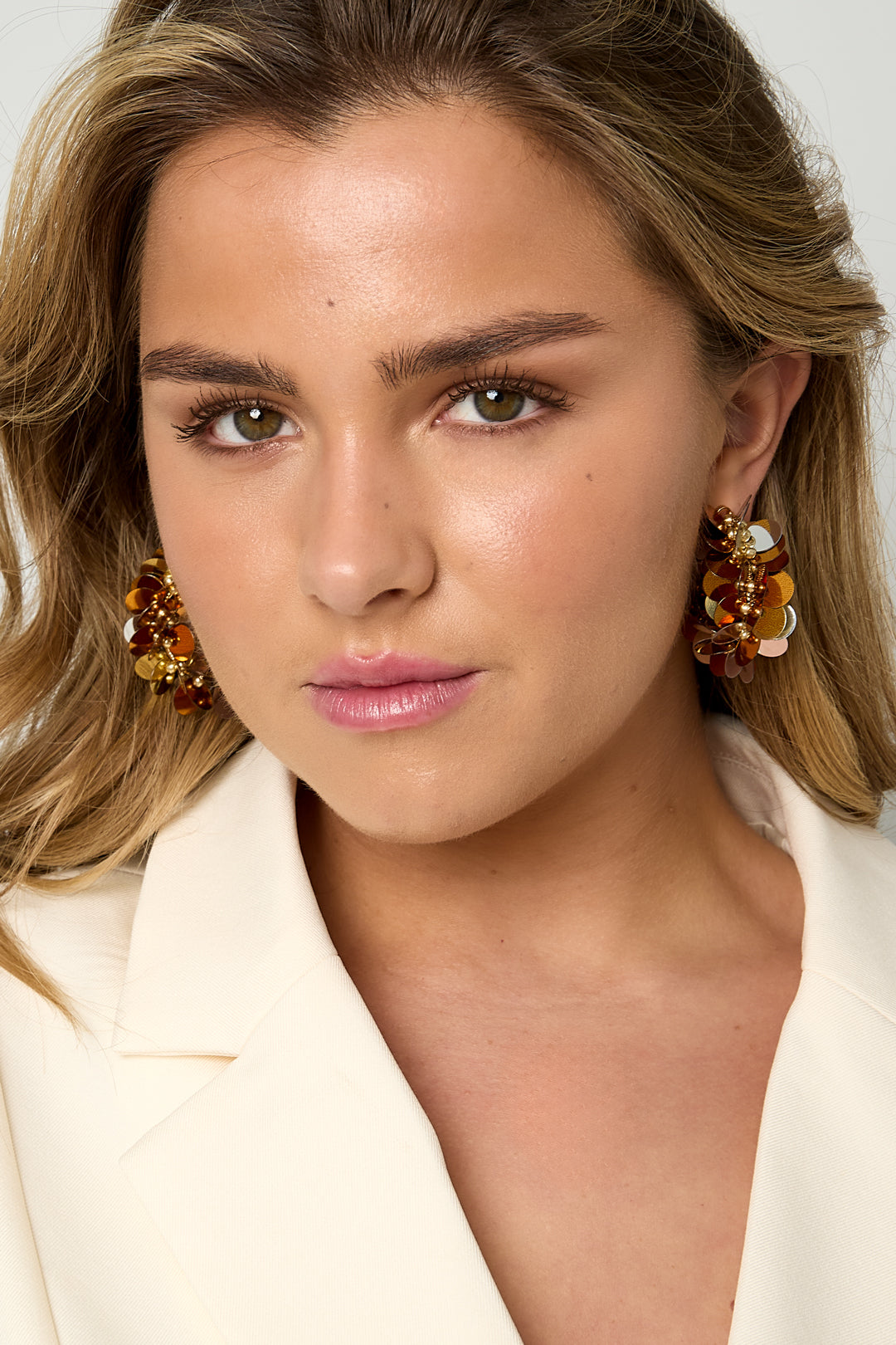 Close-up side view of gold tone sequin hoop earring on model's ear