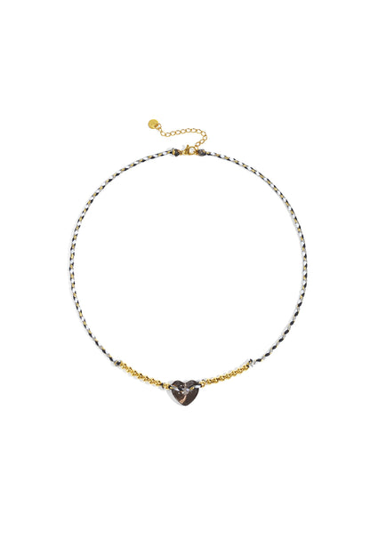 Black and white braided necklace with smoky translucent heart bead and gold-tone beads on white background