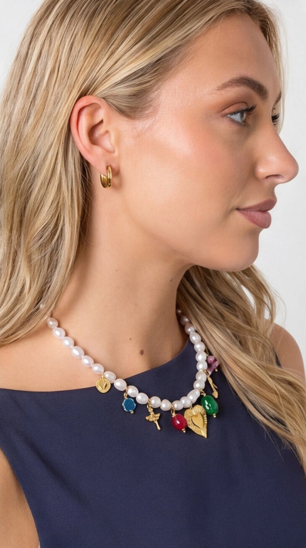 Pearl multi-charm necklace featuring colorful gemstone charms, gold-toned emblems, and a central gold heart pendant.