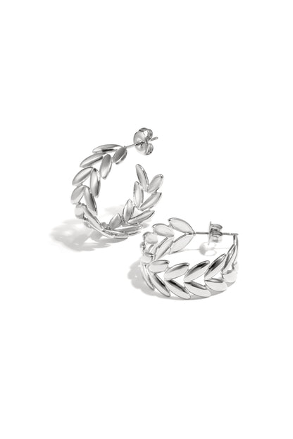 Pair of silver leaf motif hoop earrings with polished finish on white background