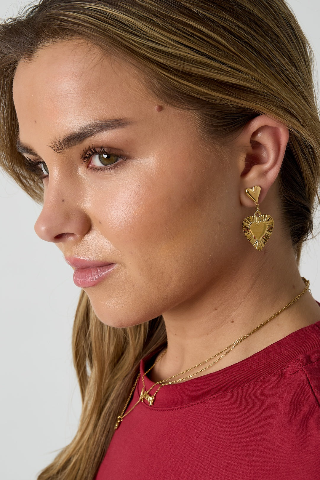 Close up side view of a woman wearing gold-tone heart drop earrings with textured edges