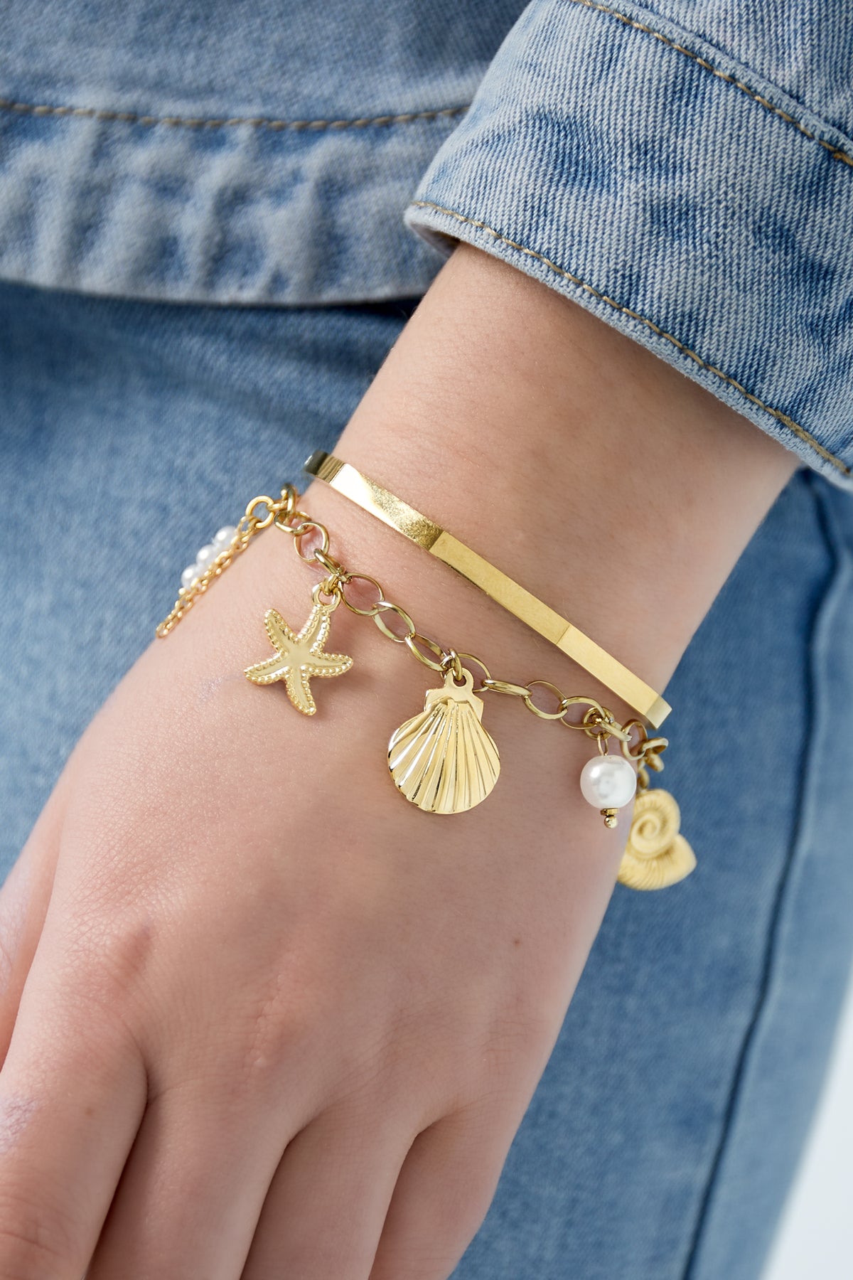 Close-up of the gold seaside charm bracelet worn with a denim jacket showing the detailed charms