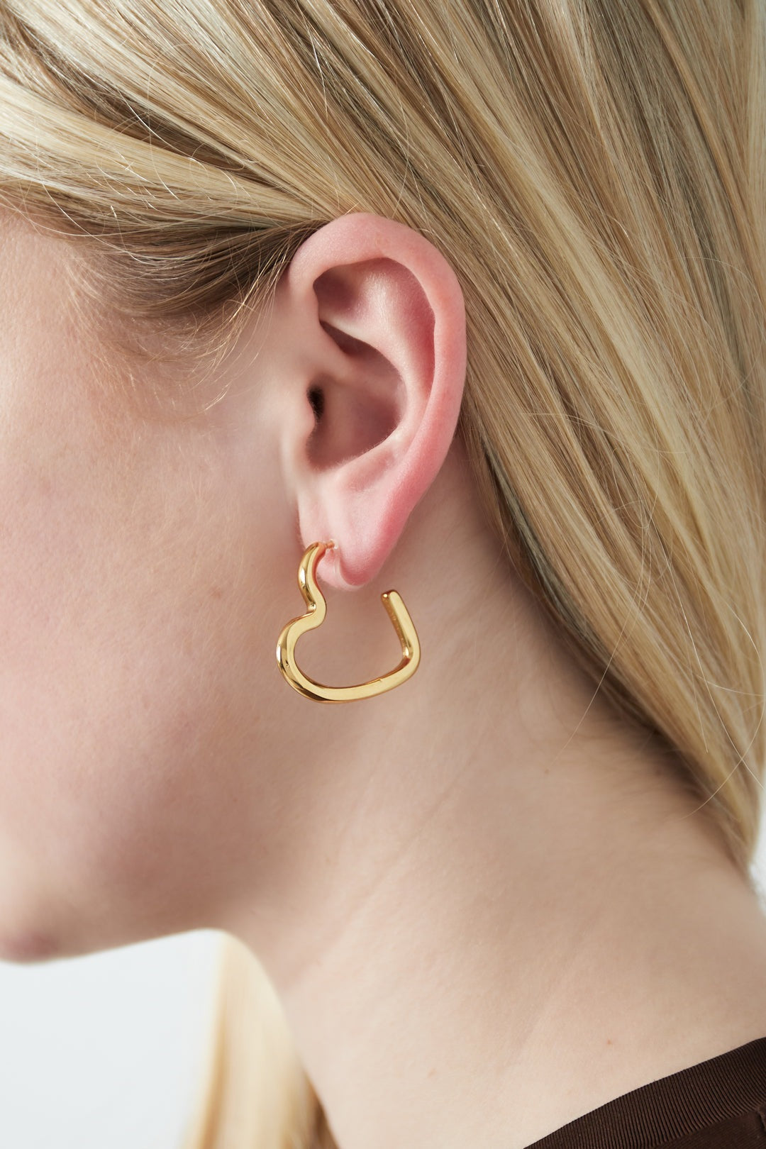 Close-up of a woman wearing glossy gold heart-shaped clip-on earring with light blonde hair