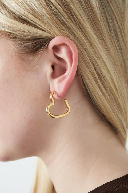 Close-up of a woman wearing glossy gold heart-shaped clip-on earring with light blonde hair