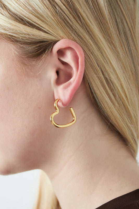 Close-up of a woman wearing glossy gold heart-shaped clip-on earring with light blonde hair