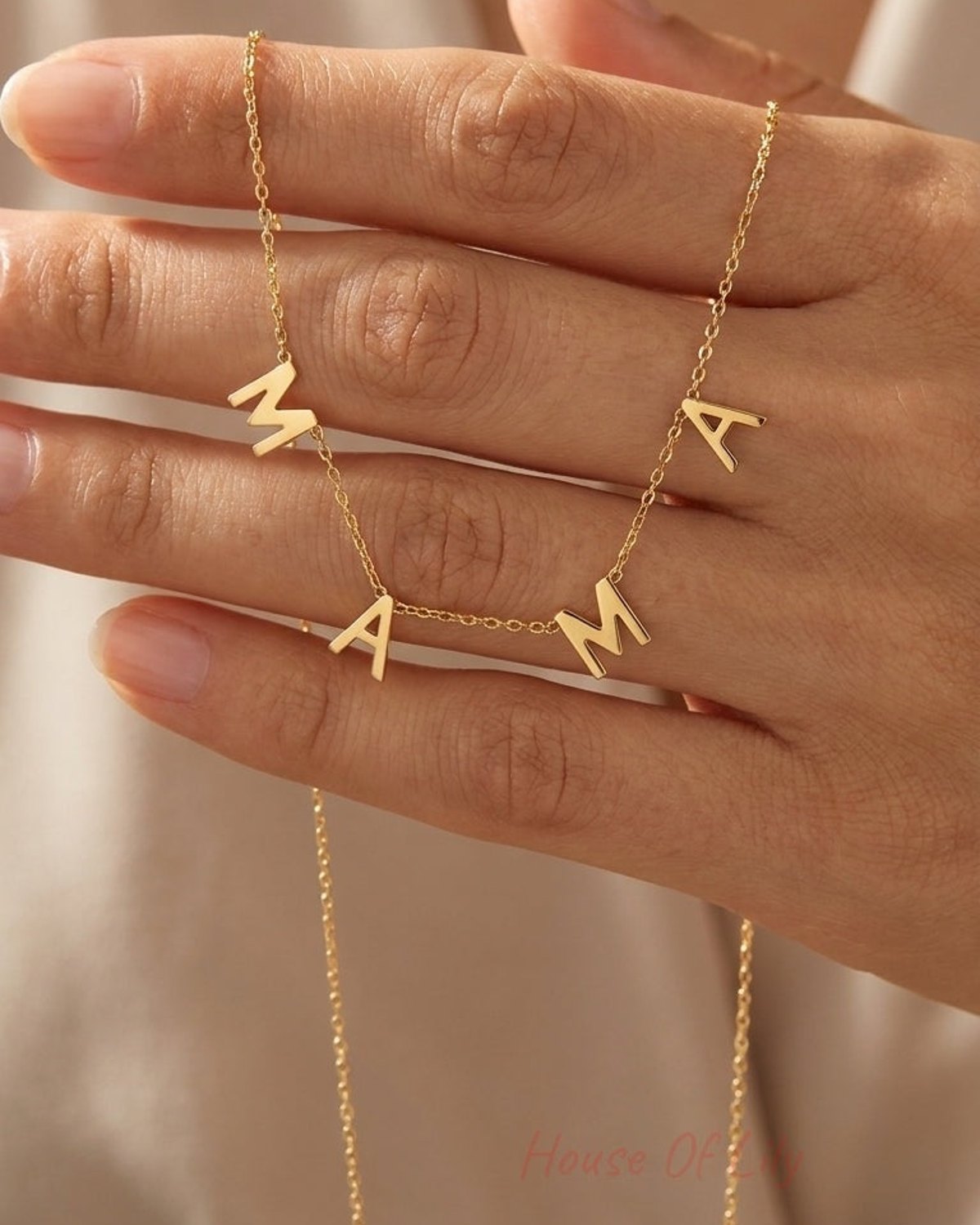 A gold chain necklace with letters spelling "MAMA" draped across a person's hand.