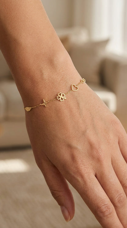 Dainty gold chain bracelet featuring a leaf, heartbeat, four-leaf clover, and heart charms on a woman's wrist.