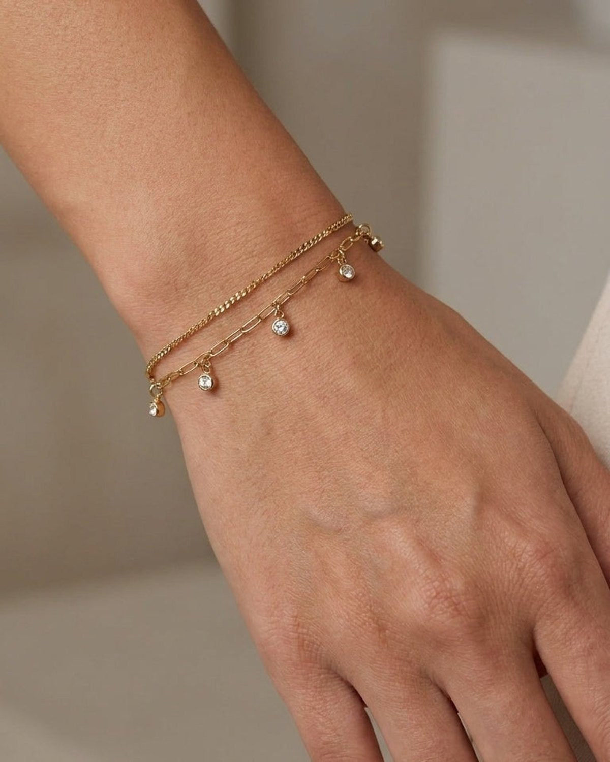 Gold multi-layered chain bracelet with dangling crystal charms worn on a wrist.