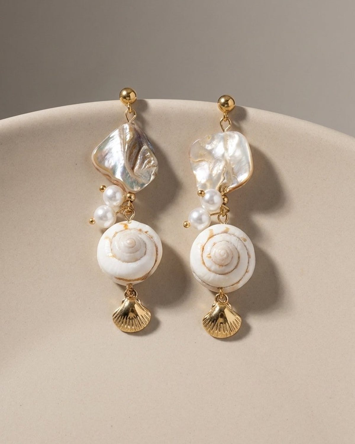 House of Lily gold earrings featuring iridescent shell slices, small pearls, spiral snail shells, and gold charms.
