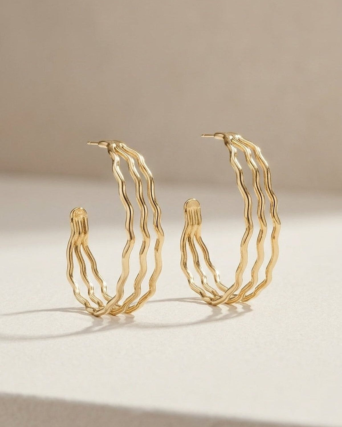 Gold-colored multi-strand wavy hoop earrings resting on a neutral surface.