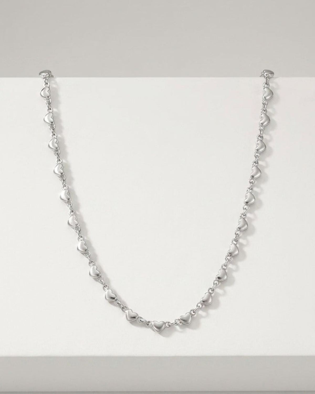 Delicate silver-toned metal necklace featuring a chain of small, repeating puffed heart charms in a romantic style.