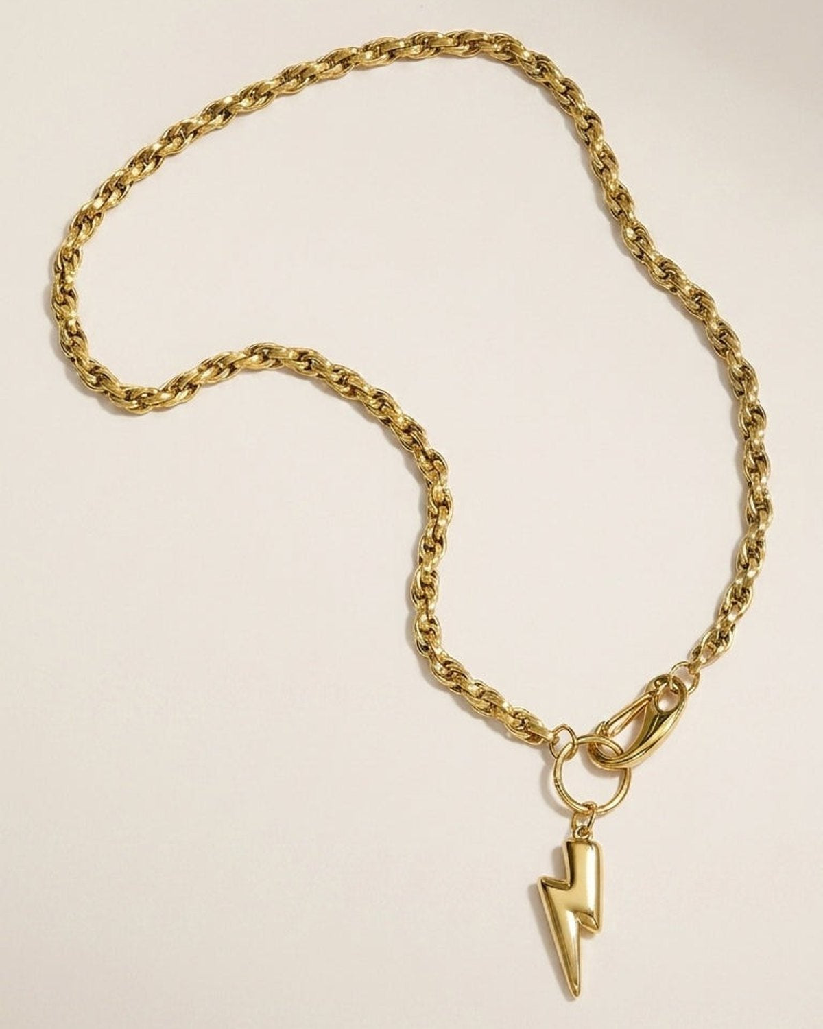 Gold tone rope chain necklace with a glossy lightning bolt pendant and clasp on a light background.