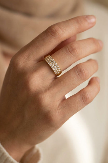Gold band ring encrusted with three rows of clear rhinestones, worn on a hand.