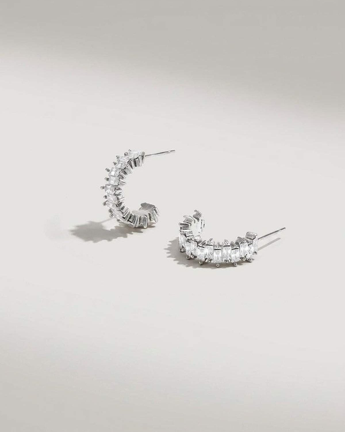 Silver hoop earrings set with alternating rows of rectangular clear stones in a zigzag design.