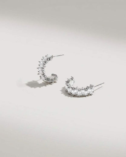 Silver hoop earrings set with alternating rows of rectangular clear stones in a zigzag design.