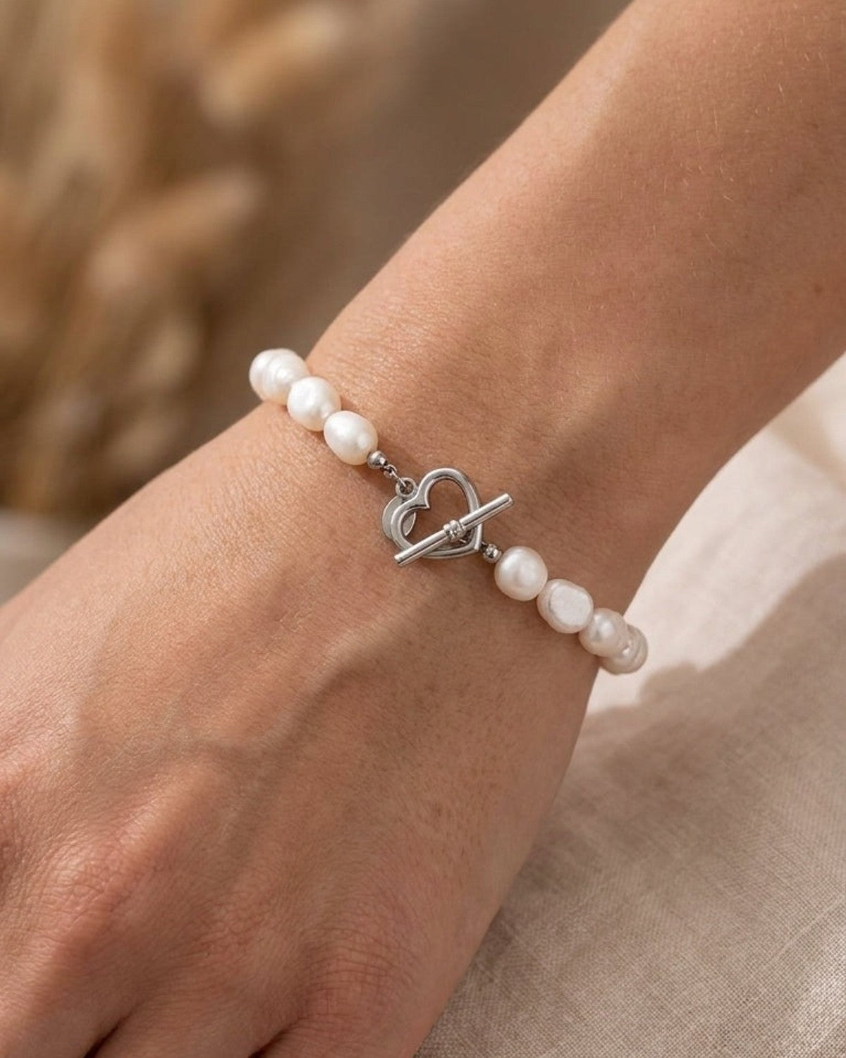 Freshwater pearl bracelet on a wrist, featuring a silver heart-shaped toggle clasp.