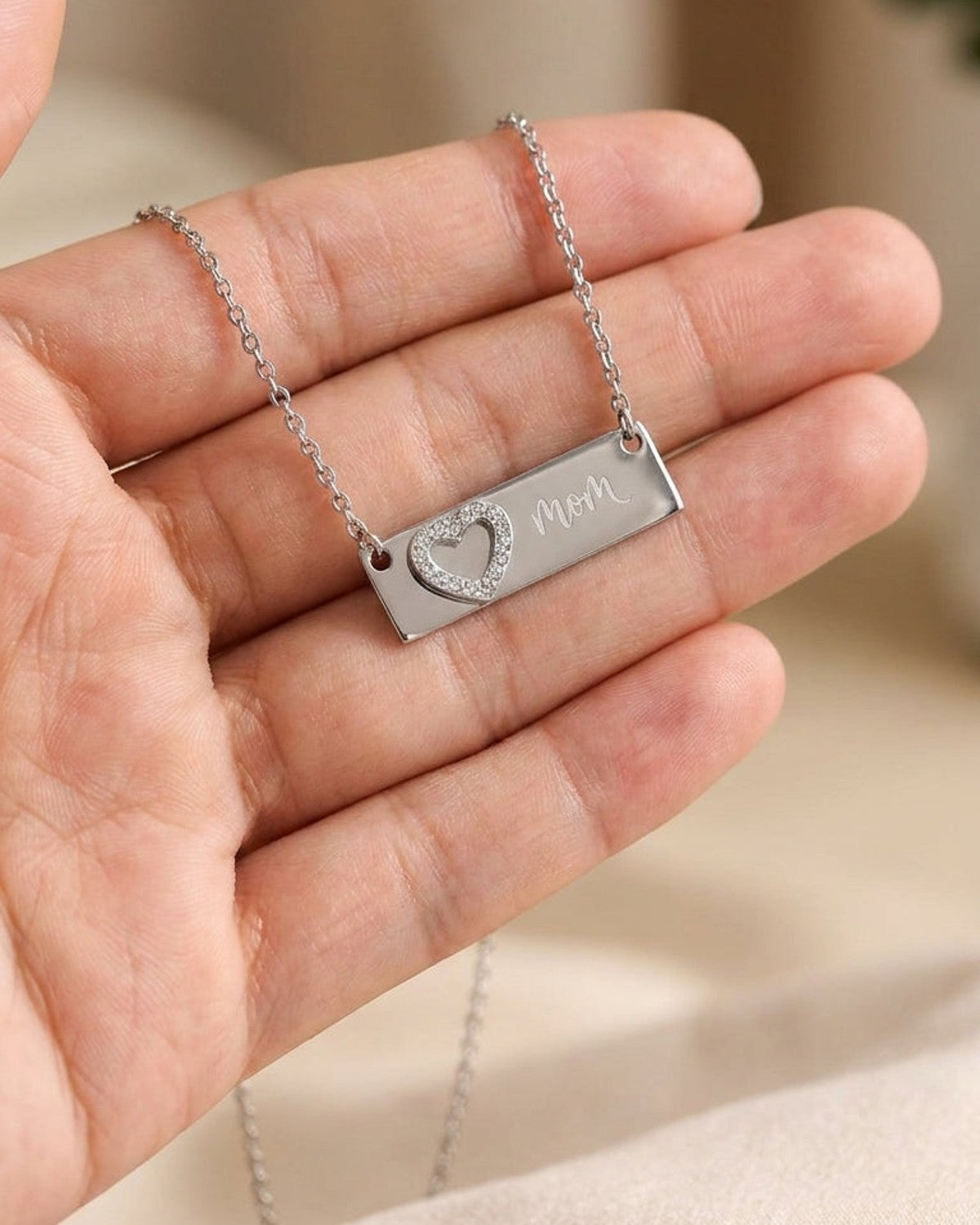 Silver chain necklace with a bar pendant engraved with "mom" and a crystal-paved heart.