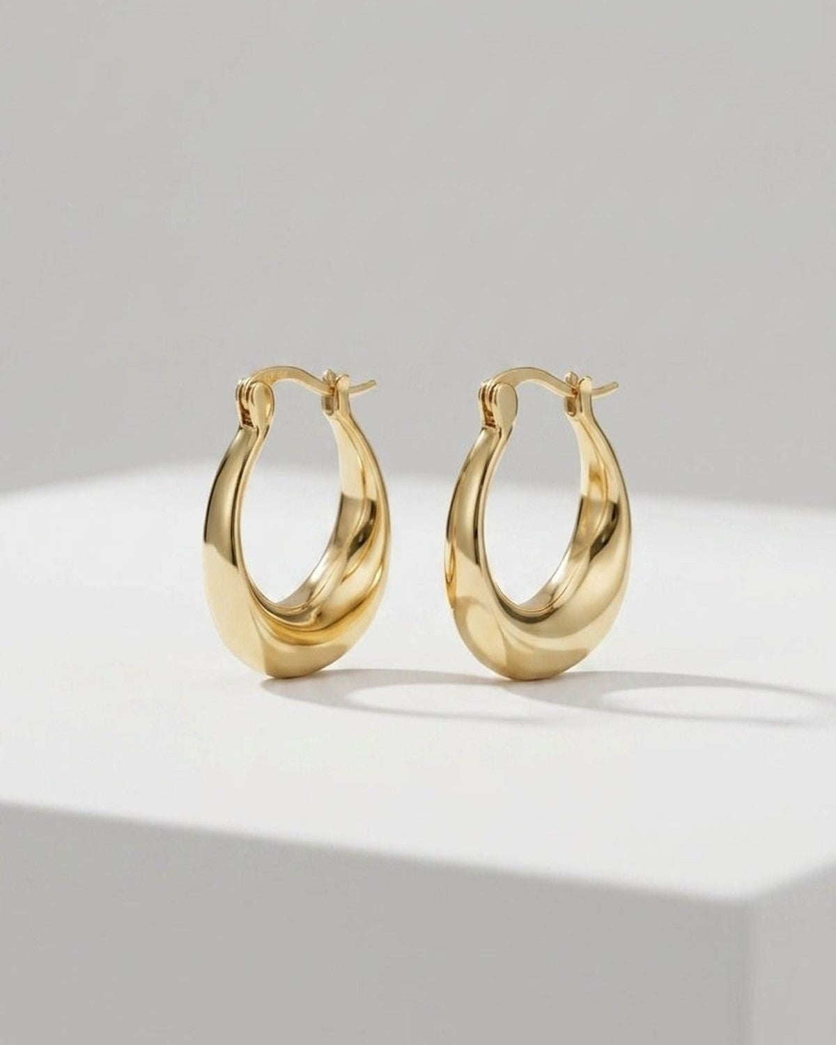 A pair of polished gold hoop earrings with a thick, organic, asymmetrical curved shape.