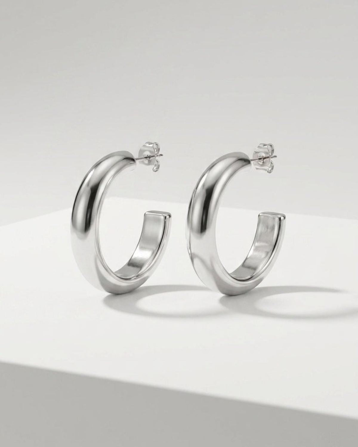 Chunky silver hoop earrings with a polished, minimalist finish on a white surface.
