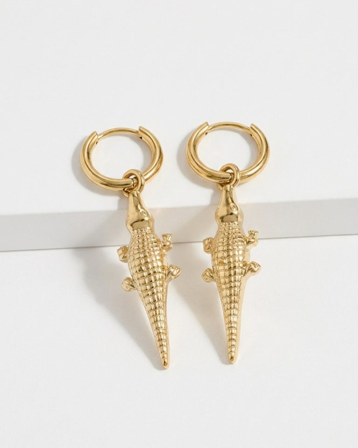 Gold-toned drop earrings featuring a textured alligator pendant hanging from a small hoop.