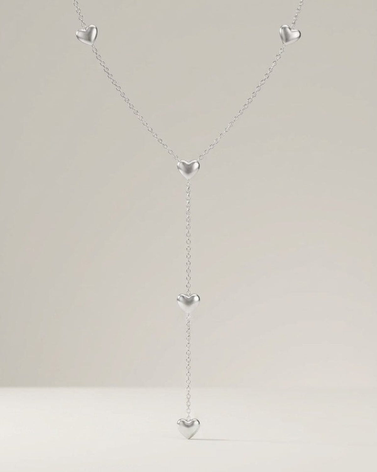 Silver y-necklace featuring a delicate chain spaced with five polished, puffy heart charms.